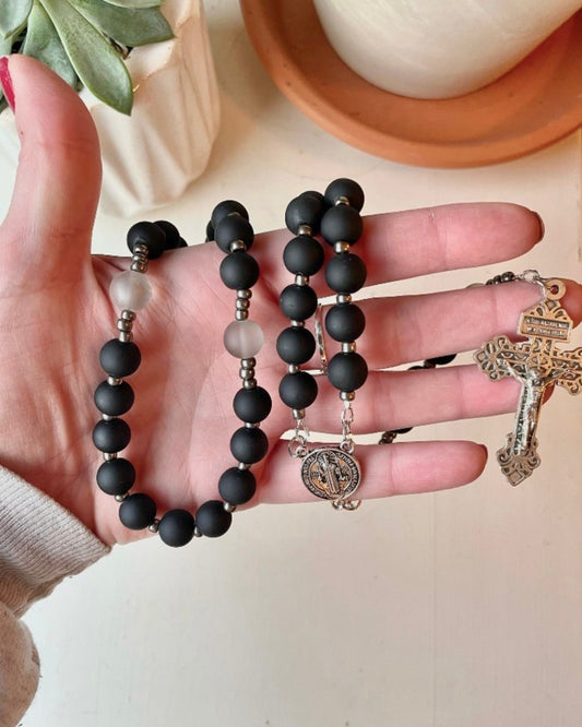 This heavyweight rosary is comprised of a matte black glass bead with a slightly rubberized texture. A light grey glass bead is added for the Our Father prayers, and is completed with silver gunmetal seed beads as spacers for a seamless experience. This set has a silver pewter St. Benedict Medal center and a Pardon Crucifix to finish it off.